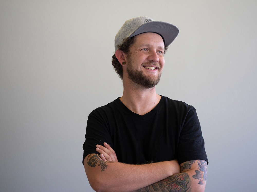 Keith McKay, Custom Branding and Merchandising Specialist at Innovative Marketing SA, smiling with arms crossed in custom branded headwear and black t-shirt.