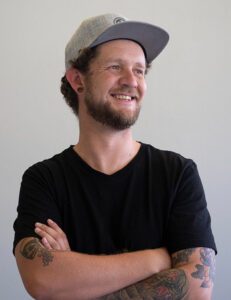 Keith McKay, custom branding and merchandise specialist at Innovative Marketing SA, smiling with arms crossed in a casual black t-shirt and grey cap.