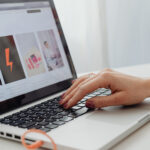 Close-up of hands typing on a laptop keyboard during digital content creation and website layout editing.